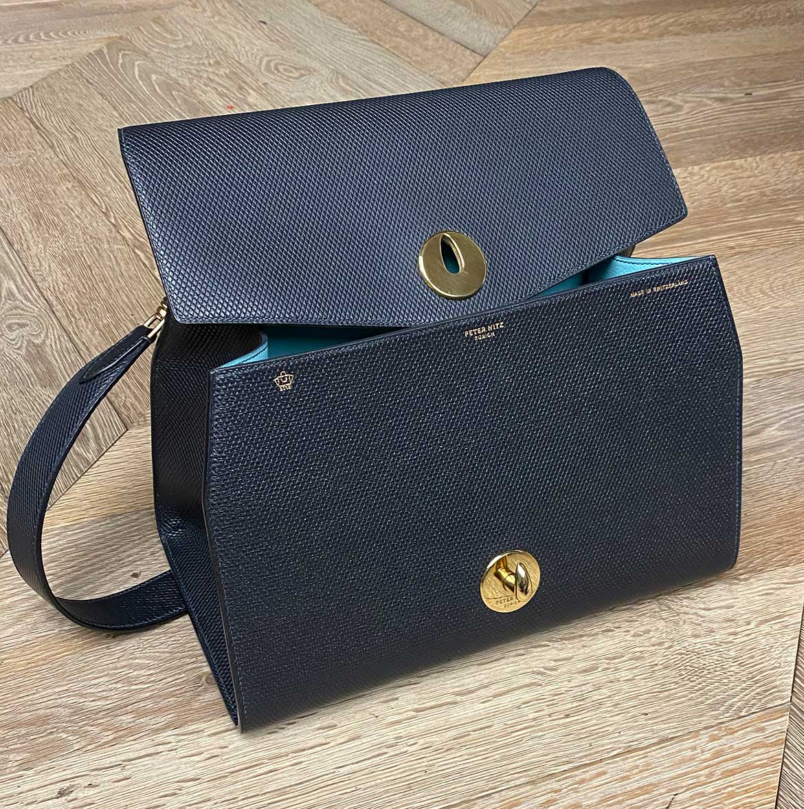A black leather shoulder bag with a flap closure and a detachable strap, featuring gold-colored hardware. The peter nitz lorin flap bag