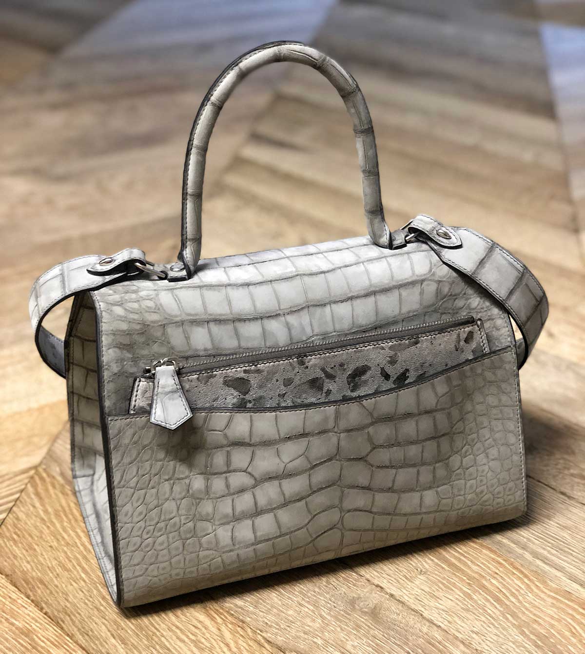 the back of the alligator lorin flap bag displayed on a wooden surface