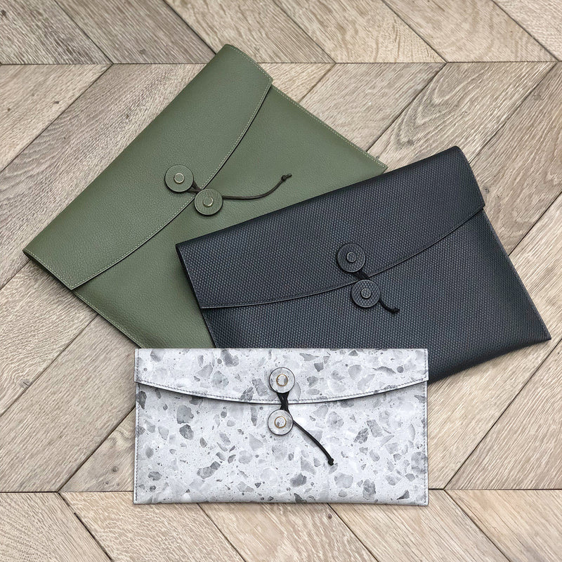 Three tether pouches in green, black, and gray colors with a snap closure, placed on a wooden surface.