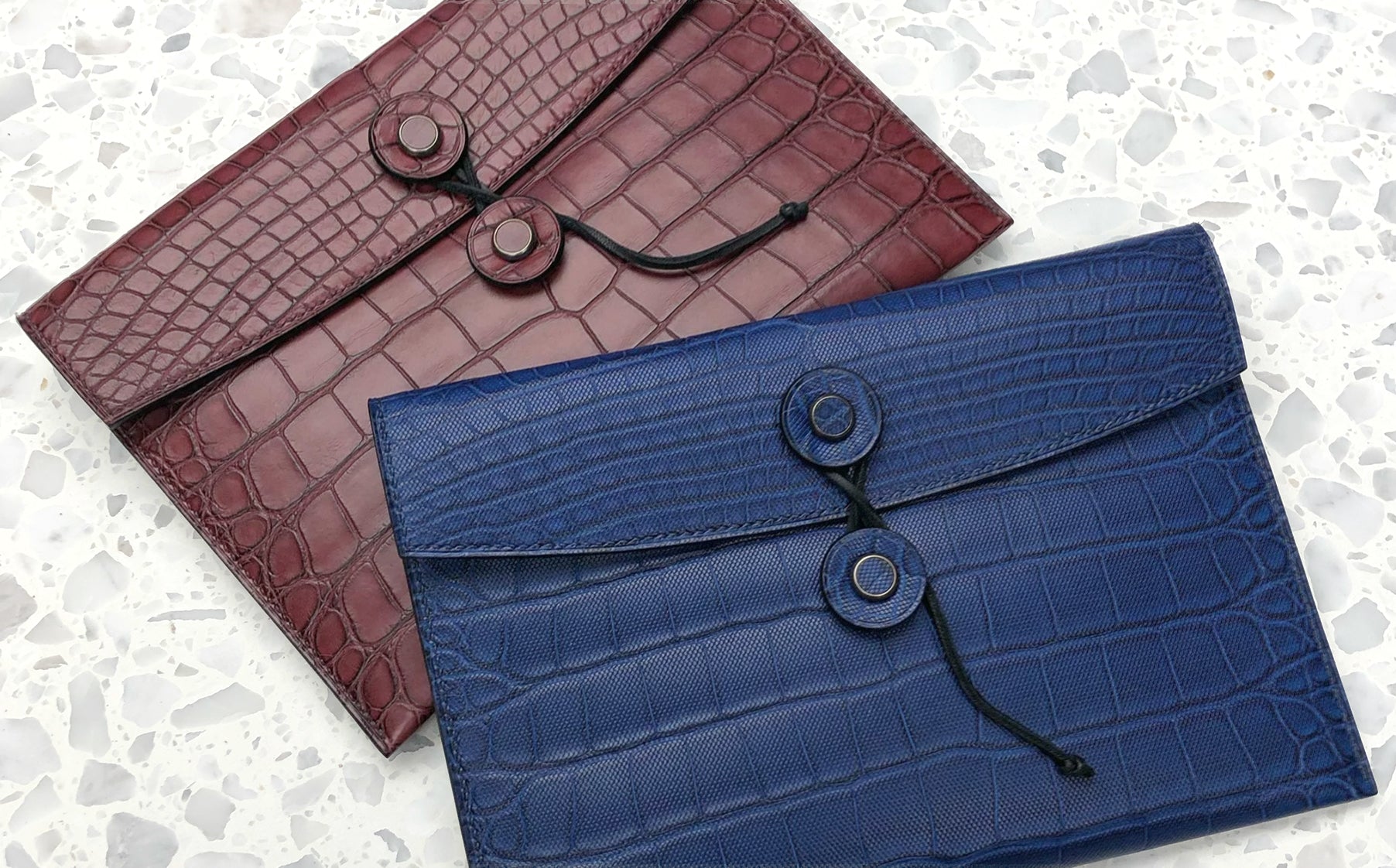 the tether pouch in alligator bordeaux and alligator blue displayed on a terrazzo marble surface