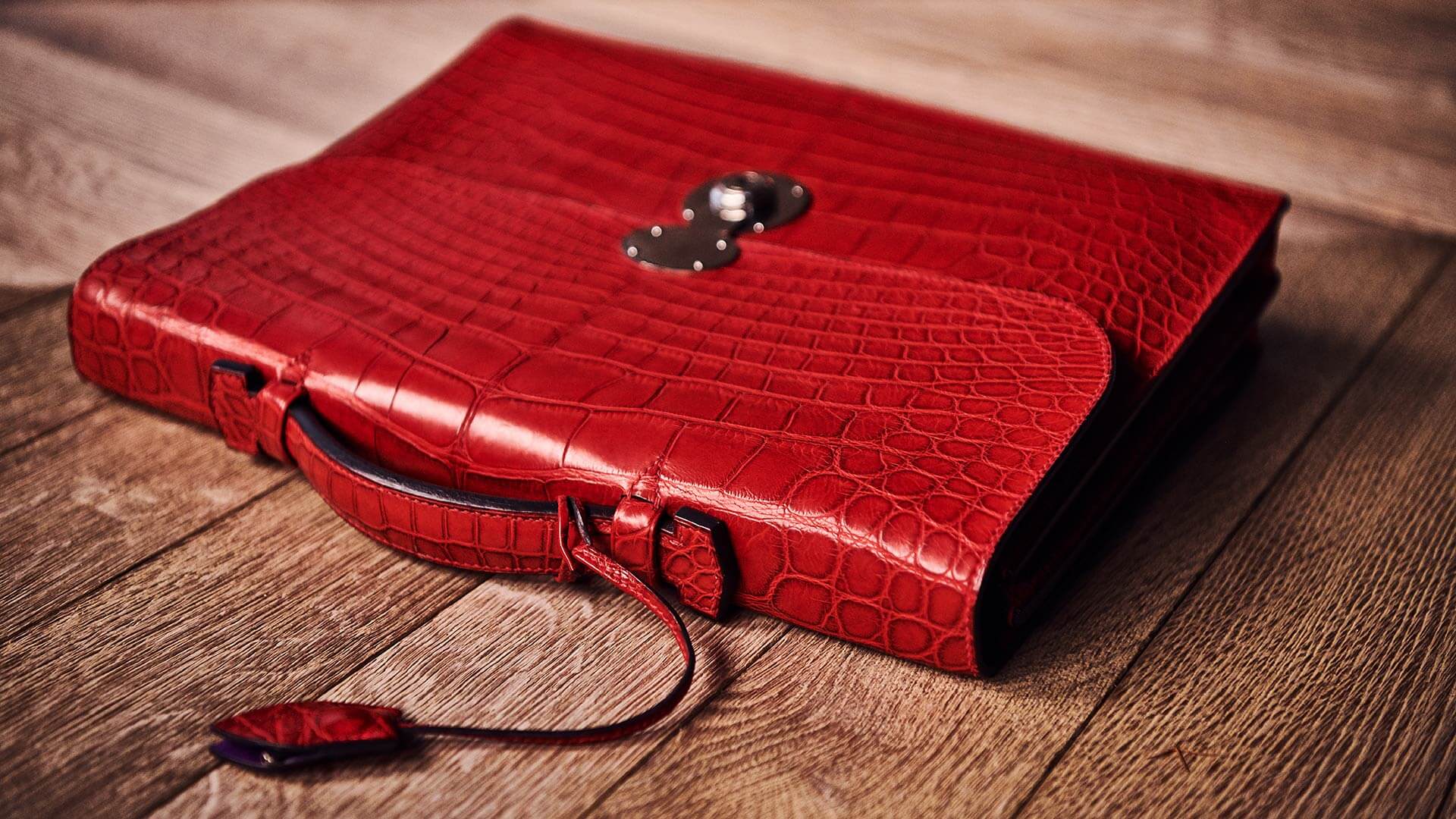 The red peter nitz hackney briefcase made out of red crocodile, placed on a wooden surface, with a small red crocodile tag