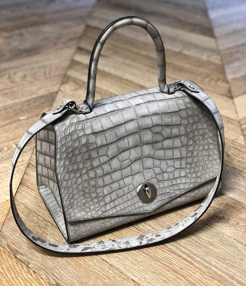 the lorin flap bag in alligator skin displayed on a wooden surface